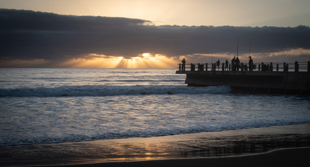 Light rays bursting from the Clouds above Fisherman at The North Beach Pier in Durban